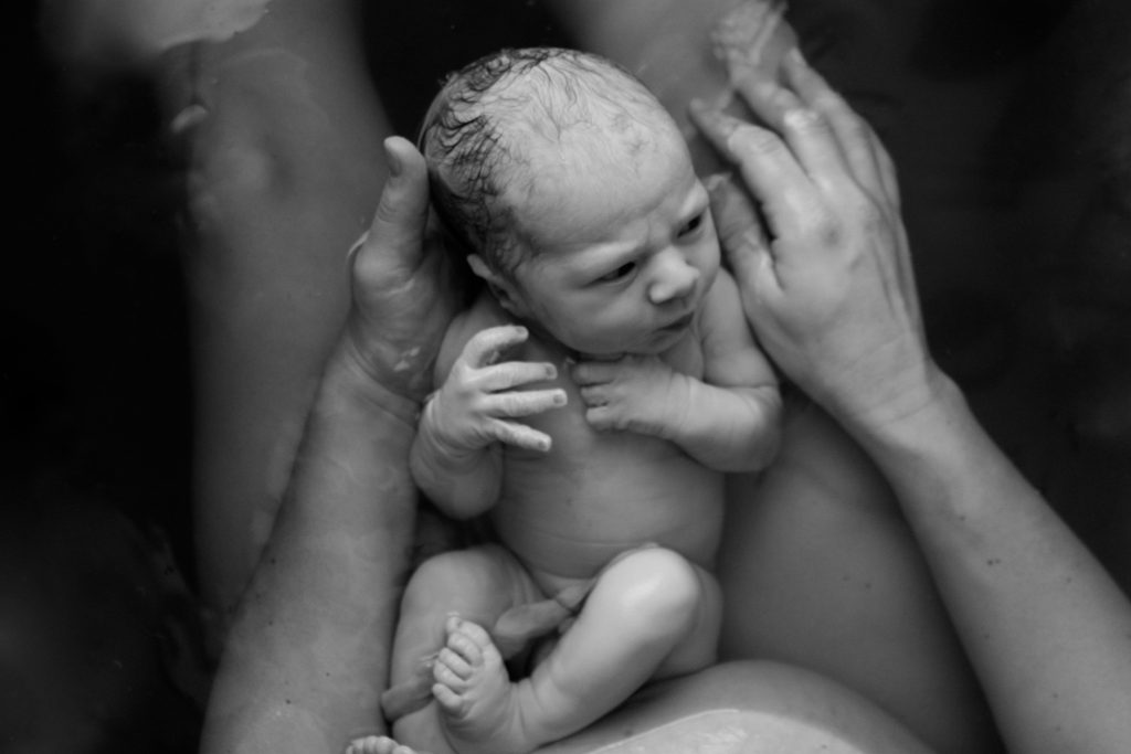 Moments after water birth, a baby on mother's lap.