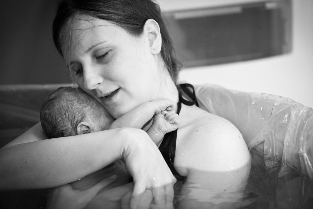 Mother embracing her newborn after giving birth at home in a water birth tub.